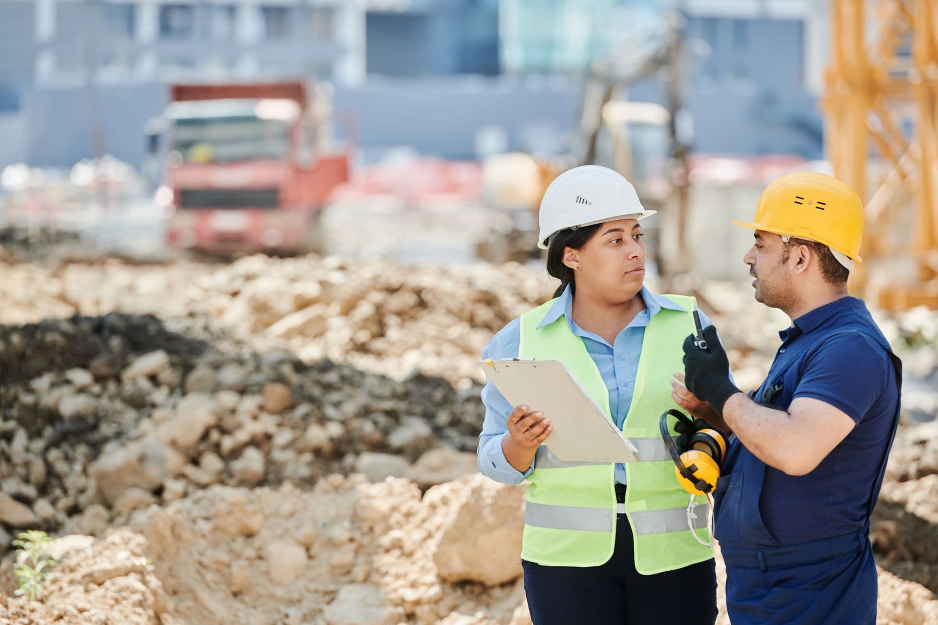 Contractor and client in hard hats reviewing work on an active excavation site with earthmoving equipment and a crane behind them