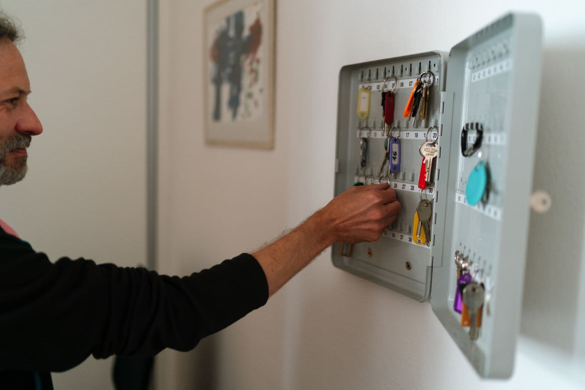 A hand reaching for keys on a numbered wall key-control cabinet stocked with color-tagged fleet vehicle keys