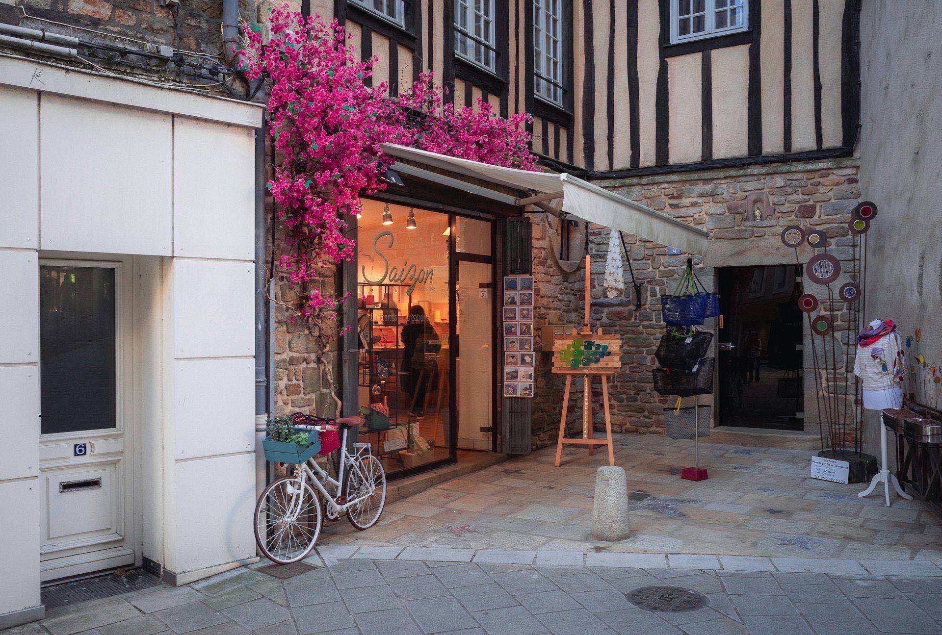 Independent boutique storefront with a lit shop window and flowering vines set on a stone-and-timber commercial street