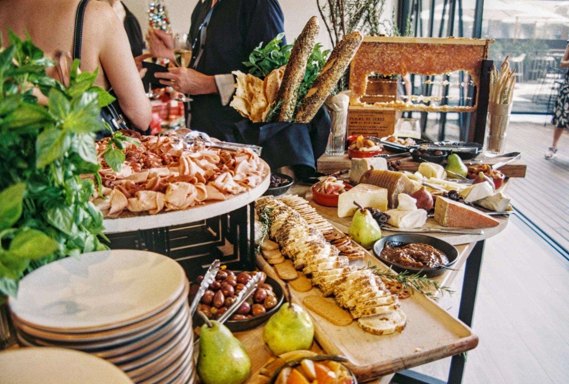 Professional catering buffet spread with charcuterie boards, artisan breads, cheese, and produce set up for an event