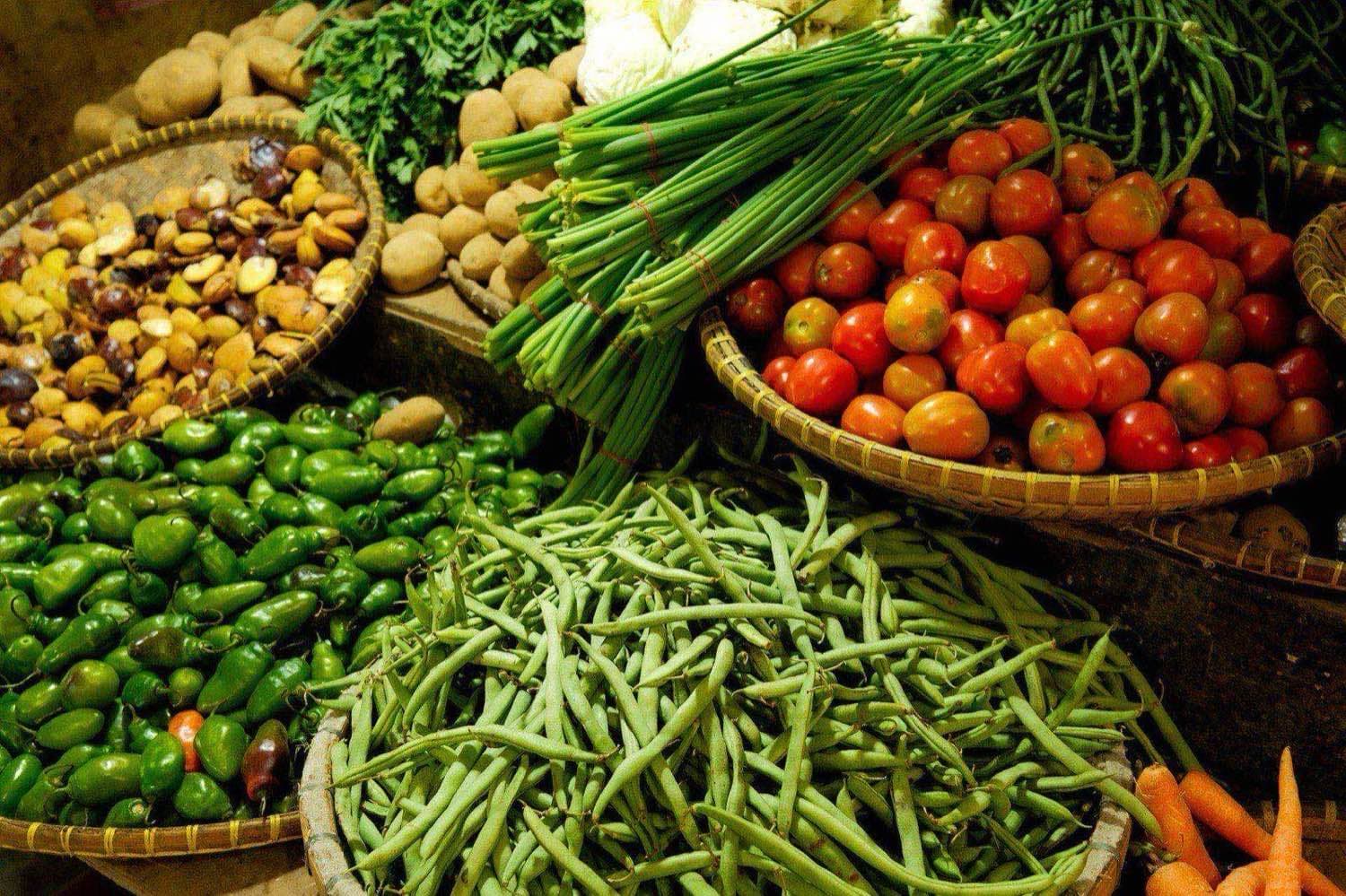 Fresh market display of tomatoes, green beans, peppers, and root vegetables arranged in wicker and crate baskets