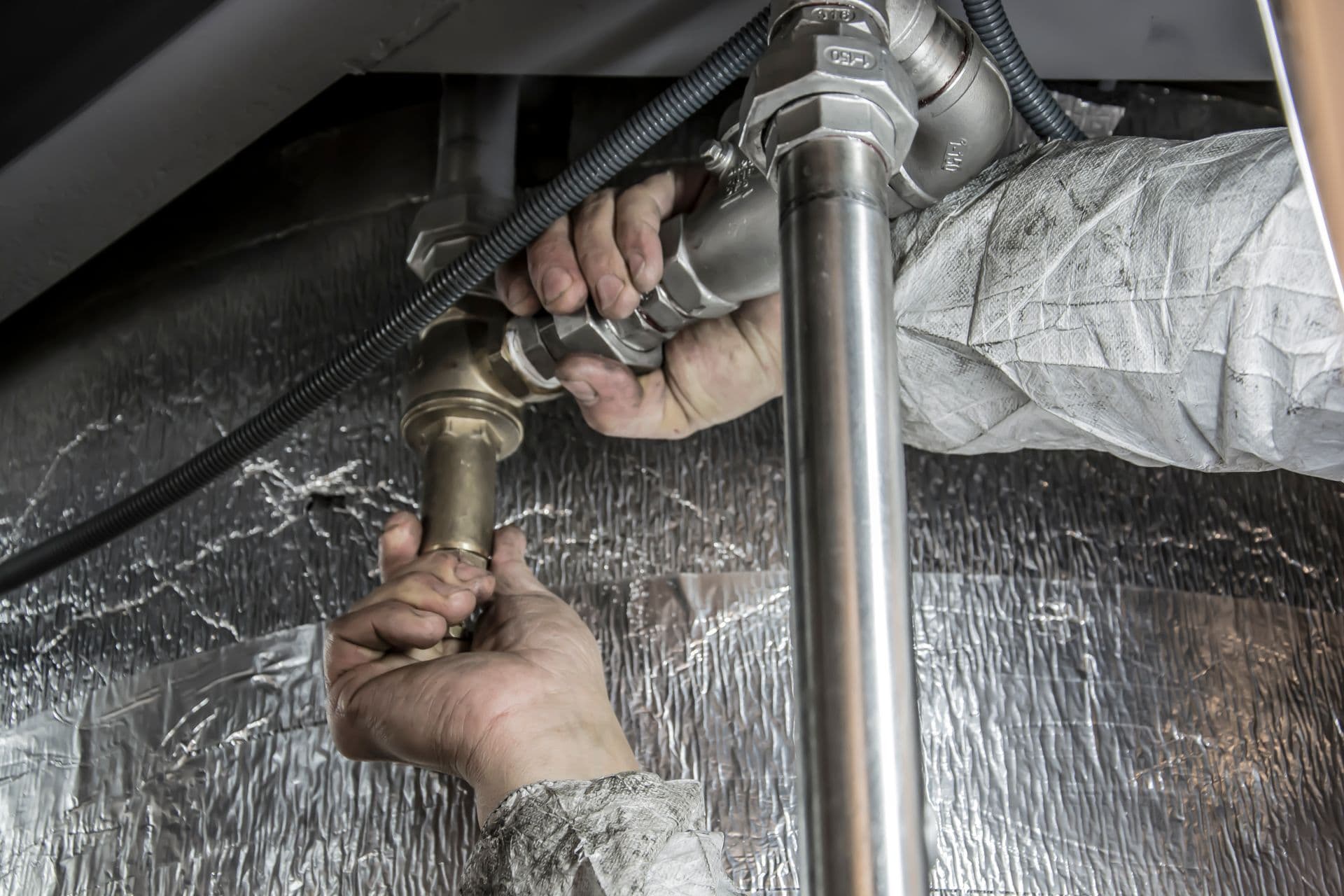 Plumber's hands installing and tightening brass and steel pipe fittings on an insulated commercial pipe system