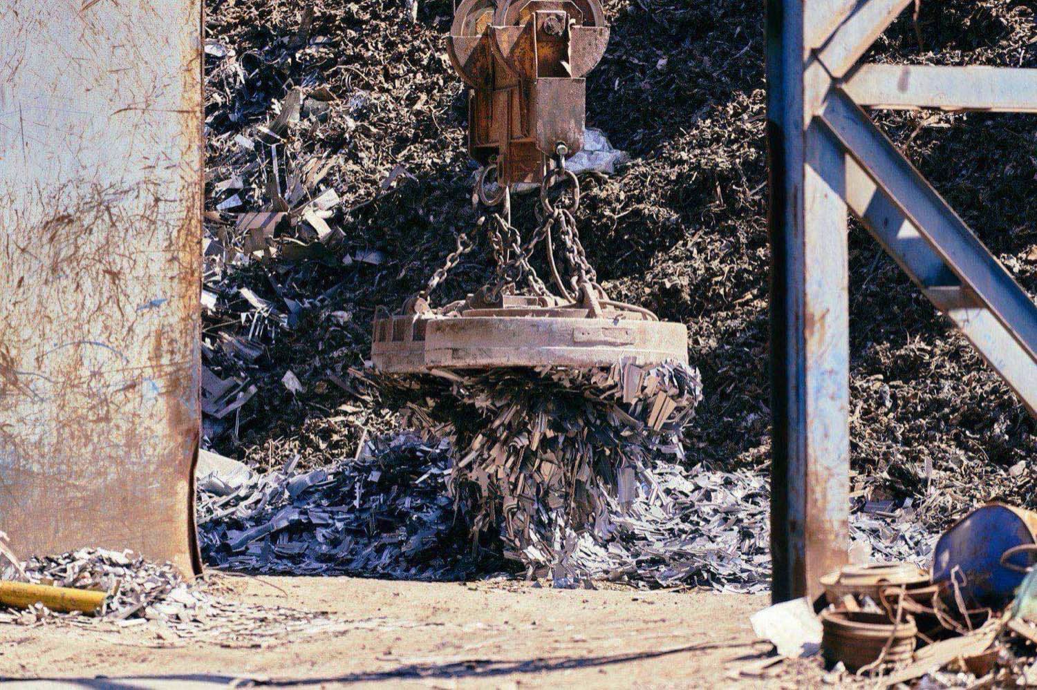 Electromagnetic crane lifting a load of crushed scrap metal at an industrial recycling and processing yard