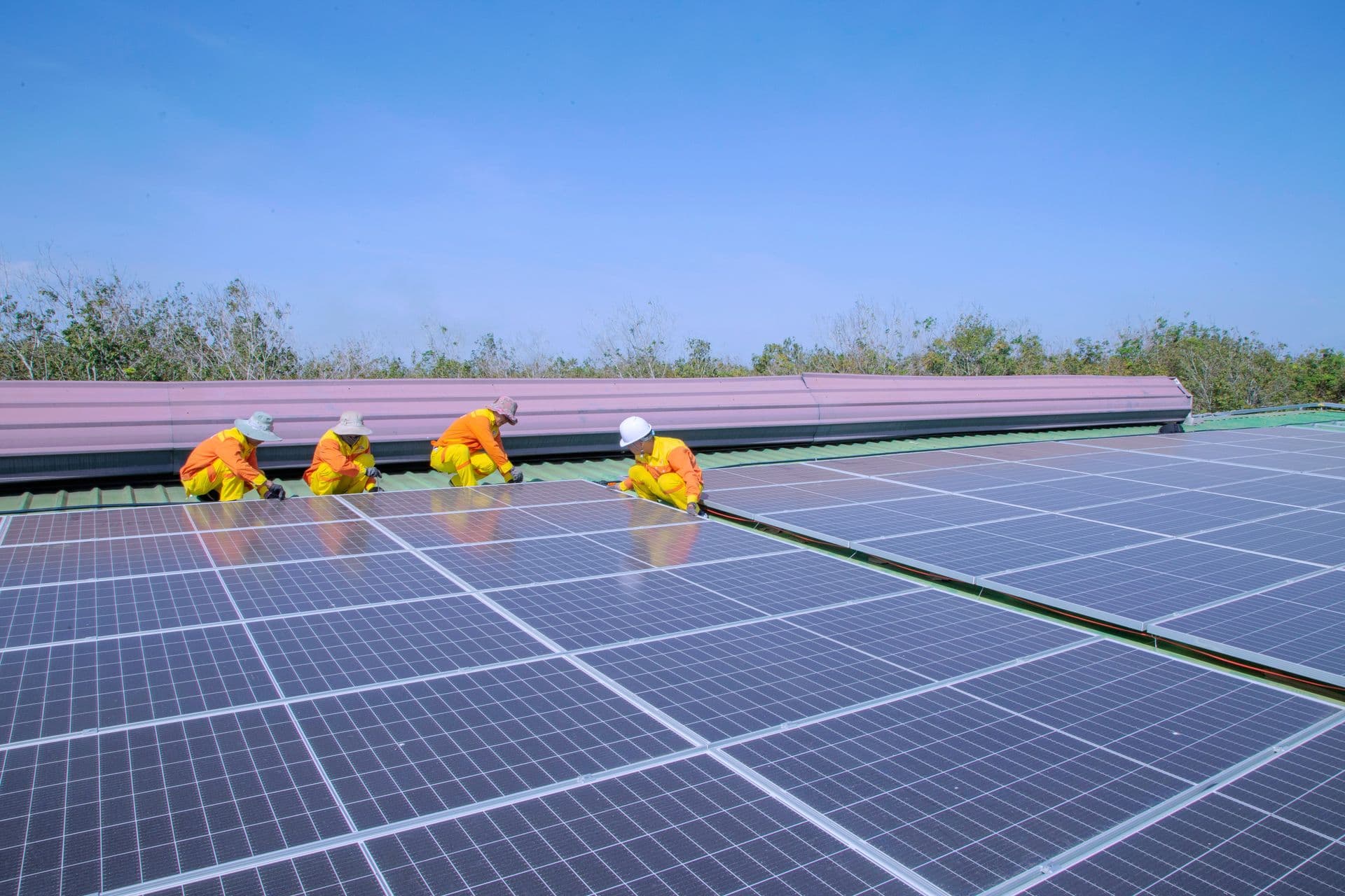 Solar installers in orange PPE and hard hats securing photovoltaic panels on a large commercial rooftop array