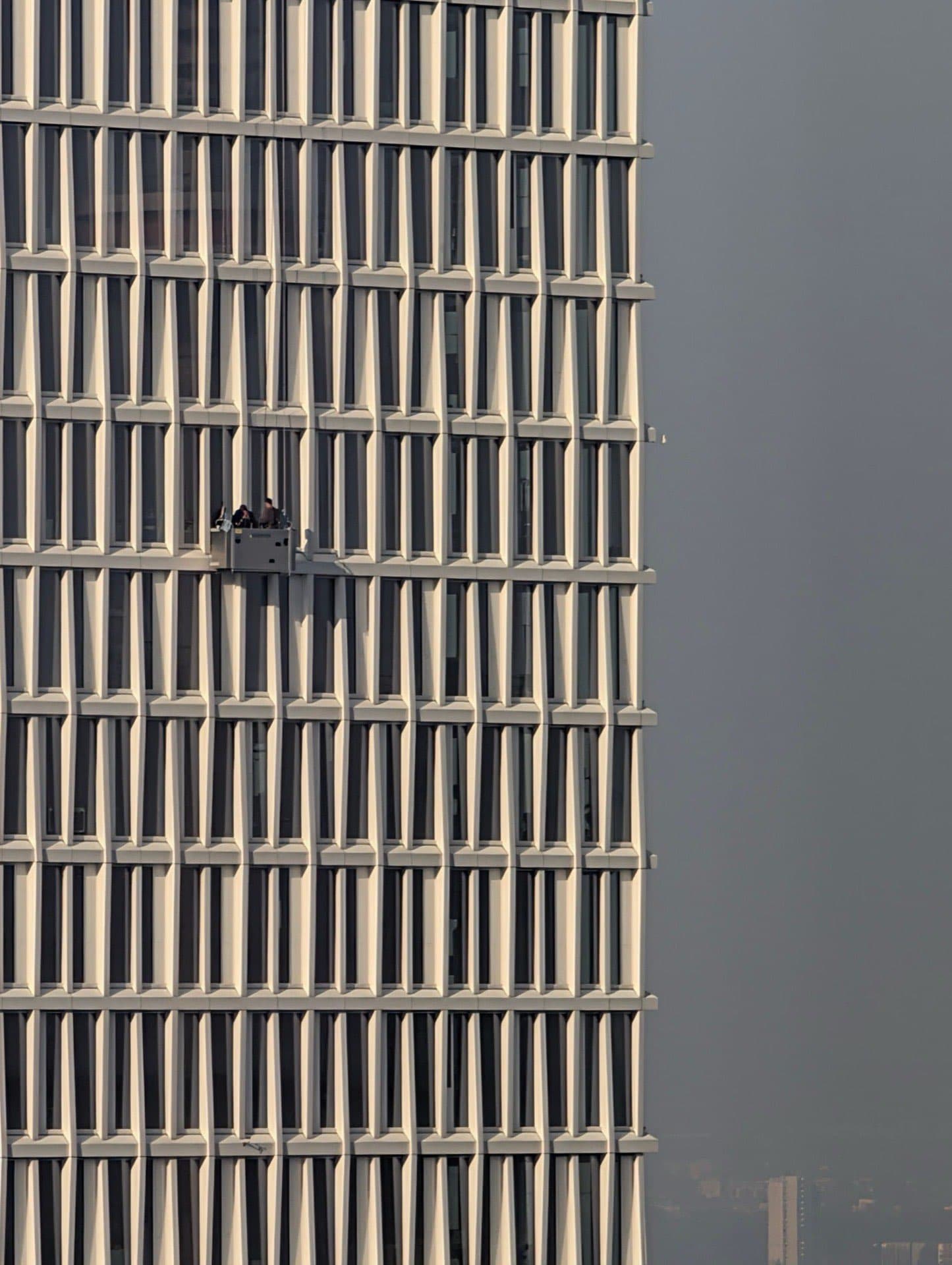 Two window cleaners on a suspended cradle platform cleaning the glass facade of a high-rise commercial building